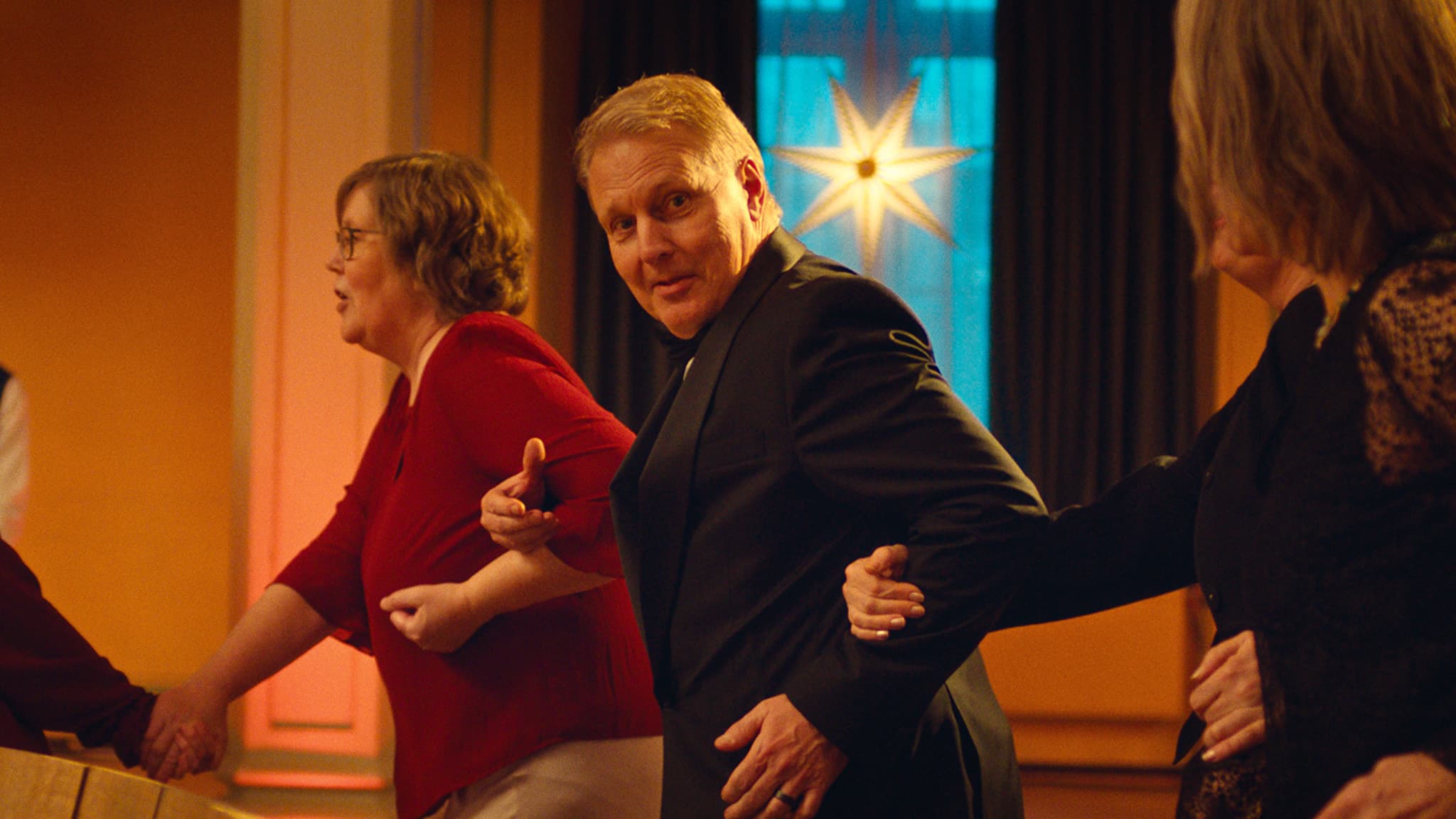 Mann løper arm i arm med to personer. En julestjerne henger bak ham.